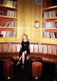 Stylish woman in a black dress relaxed on a modern couch surrounded by vinyl records, reflecting a vibrant, artistic space.