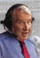 John Madden broadcasting a football game, wearing a headset and tie, showcasing his iconic commentary style.