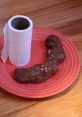 Chocolate treat shaped like poop on a red plate, next to a roll of paper towels, playful and humorous food presentation.