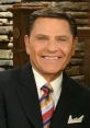 Kenneth Copeland smiles warmly, wearing a suit and tie, in front of a rustic stone backdrop, exuding charisma and positivity.