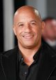 Vin Diesel smiling at a premiere event, showcasing his signature bald look and stylish black attire, exuding charisma.