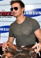 Jeremy Renner signs memorabilia at a Marvel event, promoting "Avengers: Age of Ultron" with a personalized touch.