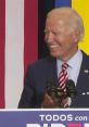 Joe Biden smiling at a podium, delivering a speech with "TODOS con BIDEN" sign, showcasing his engagement with supporters.