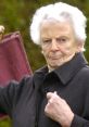 Elderly Scottish lady in a dark coat, confidently holding a bag with a serious expression, showcasing traditional culture.