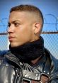 Confident individual in leather attire with a distinct earring, showcasing a bold expression against a barbed wire backdrop.