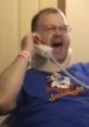 Tourettes Guy Mega passionately yells into a phone while wearing a neck brace, showcasing his unique humor and expression.