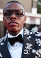 DaBaby in a stylish floral suit with oversized glasses, showcasing a bold fashion statement at a red carpet event.