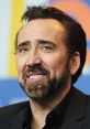 Nicolas Cage smiles during a press conference, showcasing his signature charm and distinctive beard style.