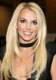 Britney Spears smiling with long blonde hair, wearing a stylish black outfit and a choker, exuding confident charm.