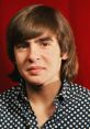 Young Davy Jones with a polka dot shirt, smiling against a red background, showcasing his iconic 1960s hairstyle.