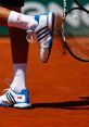 Tennis player in blue and white shoes kicks up clay on the court while preparing to swing their racket.