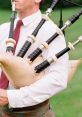 Man in a kilt playing a traditional bagpipe outdoors, showcasing the instrument's distinctive drones and chanter.