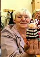 Smiling British grandma holds a knitted doll, showcasing her crafts with pride and a hint of playful attitude.