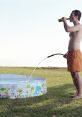 Man filling a colorful inflatable pool with water while holding a drink, enjoying a sunny outdoor day.