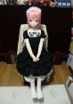 Anime-style doll with pink hair in a black dress, sitting serenely on a chair, perfect for Hentai enthusiasts and collectors.