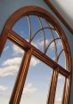 Elegant wooden arch window with detailed trim, showcasing clear blue sky and clouds, enhancing interior aesthetics.