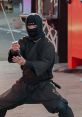 Ninja dressed in traditional black attire demonstrating sword techniques in a lively outdoor setting.