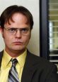 Dwight Schrute from "The Office" with a serious expression, wearing a yellow shirt and gray suit, office background.