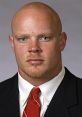 Headshot of a professional man in a suit with a red tie, featuring a bald head and piercing green eyes, exuding confidence.