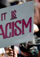 Sign reading "It Is Racism," held during a protest against racism, highlighting social justice issues.