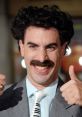 Borat character gives a thumbs up with a big smile, showcasing his iconic mustache and suit at a lively event.