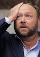 Alex Jones looking distressed, hand on forehead, during a tense moment in a public appearance or court hearing.