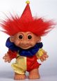 Colorful troll doll with red hair, clown outfit, and cheerful expression, embodying nostalgic charm and playful whimsy.