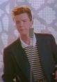 Rick Astley performing his hit song, iconic for the Rick Roll meme, wearing a striped shirt and suit, singing passionately.