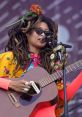 Colorful performer with dreadlocks playing guitar at a vibrant music festival, capturing the spirit of live entertainment.