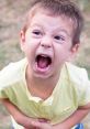 Young boy screaming with a shocked expression, depicting intensity and emotion in a vibrant outdoor setting.