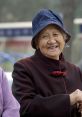 Smiling elderly Chinese woman wearing a traditional coat and denim bucket hat, conveying warmth and joy in her expression.