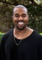 Kanye West smiling while wearing a black shirt and gold necklace, surrounded by greenery in a sunny outdoor setting.