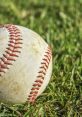 Close-up of a worn baseball resting on lush green grass, showcasing its iconic stitching and weathered surface details.