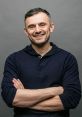 Gary Vee smiling, arms crossed, wearing a navy hoodie against a gray backdrop, exuding confidence and approachability.