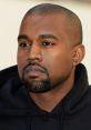 Kanye West with a serious expression, wearing a black hoodie, featuring closely cropped hair and a well-groomed beard.