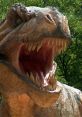 Detailed close-up of a roaring dinosaur sculpture showcasing sharp teeth and textured skin in a lush green environment.