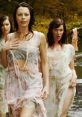 Three enchanting sirens in flowing dresses wade through a forest stream, evoking a mystical and alluring atmosphere.