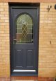 Elegant dark front door with decorative glass panel, enhancing curb appeal against a brick wall background.