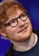 Ed Sheeran with glasses, smiling at an event, showcasing his signature style and charismatic personality.