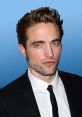 Robert Pattinson exudes charisma in a formal suit, showcasing his signature style against a blue background.