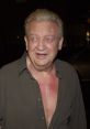 Rodney Dangerfield smiling, wearing an unbuttoned shirt, showcasing his distinctive comedic persona and striking facial expressions.