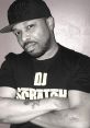 DJ Scratch poses confidently in a black t-shirt and cap, showcasing his passion for music and turntablism.