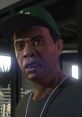 Lamar Davis from GTA V with an intense expression, wearing a green cap and black shirt. Intrigued character moment.