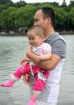 Father holding smiling baby by the lakeside, showcasing a joyful moment and bonding experience in a serene environment.