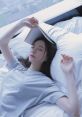 Young woman relaxing on a bed with a book resting on her forehead, embodying tranquility and serenity in a cozy setting.