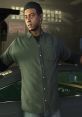 Character from GTA 5 wearing a green shirt, gesturing in a garage with classic cars in the background.