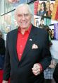 Ed McMahon smiling at a red carpet event, wearing a black suit and red shirt, exuding charisma and charm.