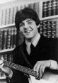 Paul McCartney smiling while playing a bass guitar, with bookshelves in the background, showcasing his musical talent.