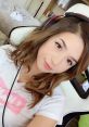 Pokimane wearing headphones, smiling at the camera, surrounded by a cozy gaming setup in her stylish room.