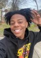 Young man with stylish dreadlocks smiles in a casual "IShowSpeed" hoodie, showing vibrant personality outdoors.